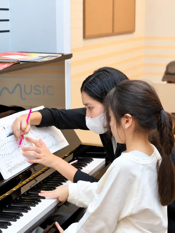 ครูสอนนักเรียนอ่านโน้ตเปียโนและวางนิ้วบนคีย์อย่างใกล้ชิด