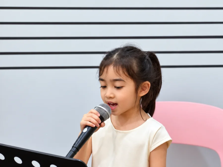 นักเรียนเด็กเล็กฝึกร้องเพลงกับไมโครโฟนในห้องเรียนร้องเพลงของ Music Mastery